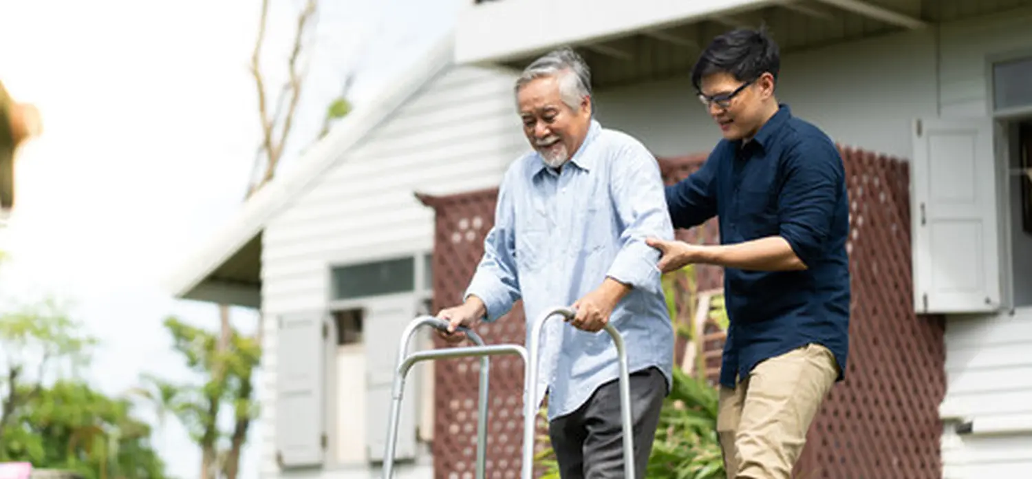 Älterer asiatischer Vater und erwachsener Sohn gehen im Hinterhof spazieren. Positiver asiatischer Pfleger hilft Patienten