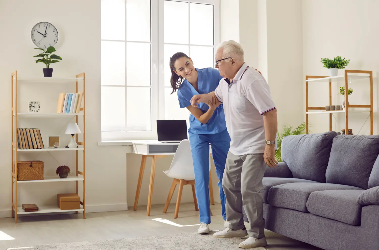 Das Leben eines Rentners in einem modernen Pflegeheim. Freundliche junge Pflegerin, die sich um einen älteren Mann im Pflegeheim kümmert, hilft ihm beim Aufstehen vom Sofa. Altenpflegekonzept.